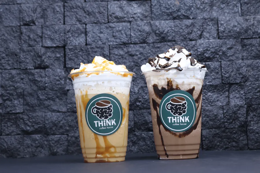 Two Think Coffee House iced frappuccinos, caramel and chocolate, against a stone wall