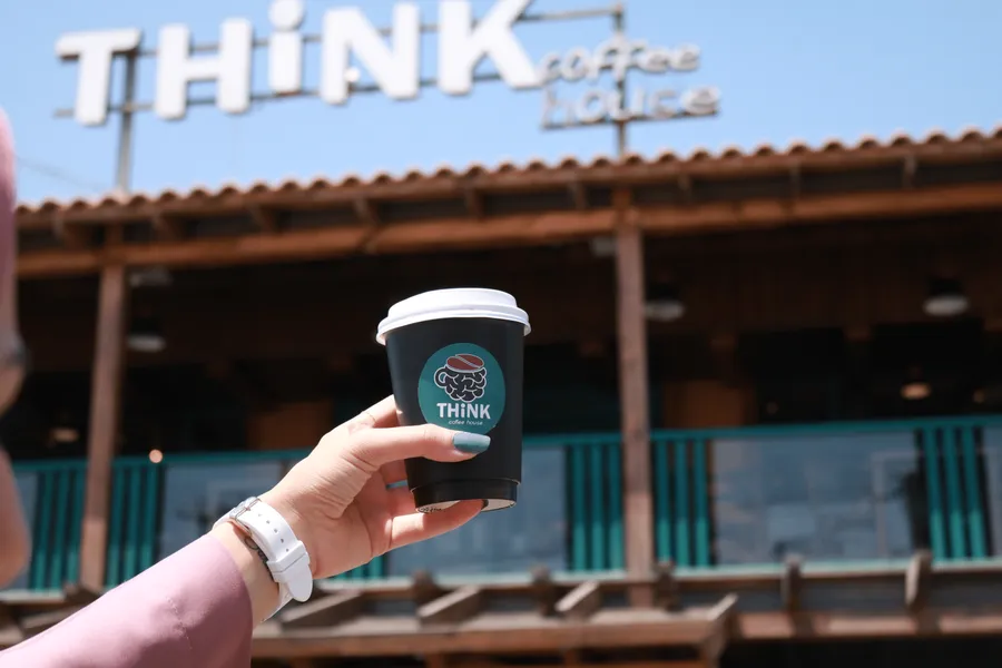 A hand holding a Think Coffee House takeaway cup outside the café
